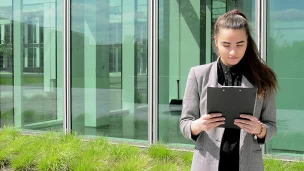 Business woman look to clipboard(paper) then smiles before business building - Footage, Video
