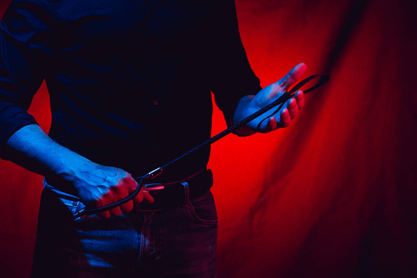 sexy muž drží bdsm bičík na červeném pozadí - Fotografie, Obrázek