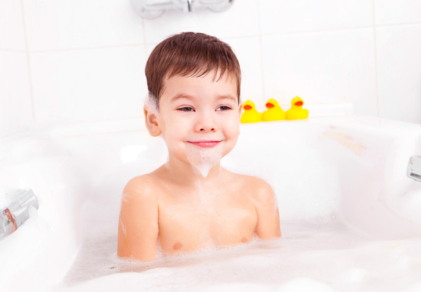Cute four year old boy taking a relaxing bath with foam - Fotó, kép