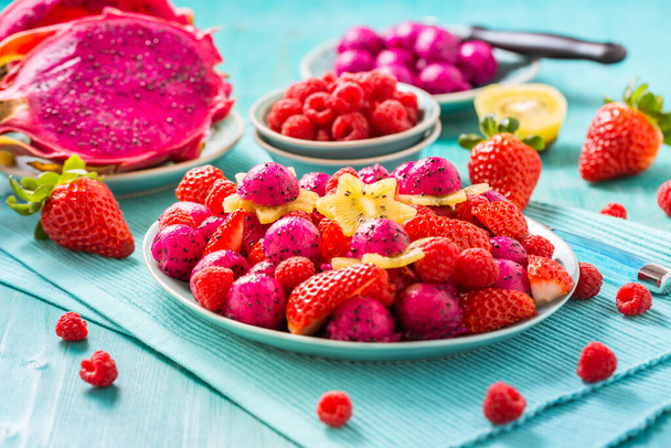 Fresh dragon fruit salad with strawberries, raspberries and start fruit (carambola) on cyan background - Photo, Image