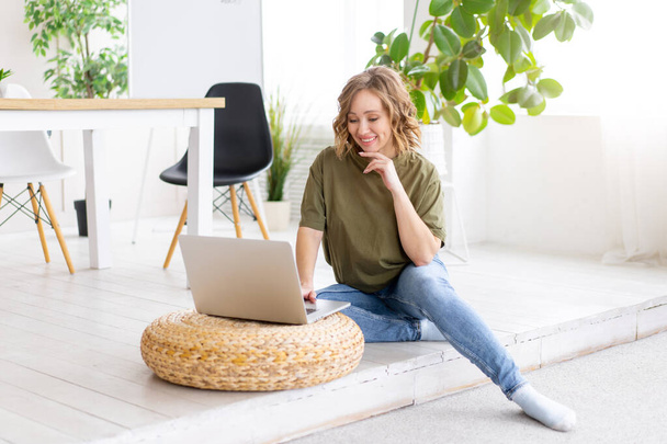 Frau benutzt Laptop-Computer, während sie zu Hause am Boden sitzt. Freiberuflerin arbeitet von zu Hause aus Fernstudentin entspannt und schaut Unterricht auf Videokonferenz - Foto, Bild