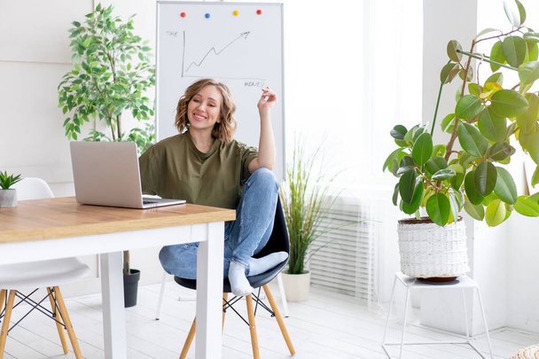 Business woman using laptop sitting desk white office interior with houseplant looking Business people Business person Online, Young and successful Dresed green shirt blue jeans barefoot relaxing  - Фото, зображення
