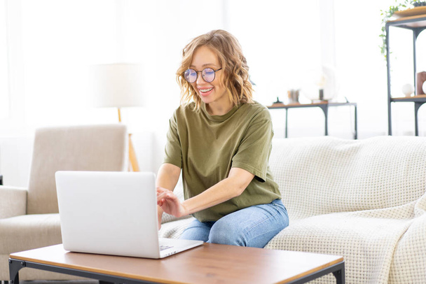 Woman with glasses use laptop typing keyboard sitting couch big window background home interior Freelance female working from home Distance learning student relaxing watch lessons video conferenc - Φωτογραφία, εικόνα
