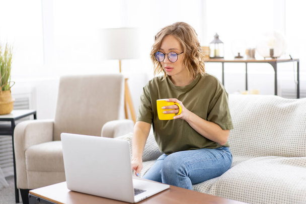 Woman with glasses use laptop typing keyboard sitting couch big window background home interior Freelance female working from home Distance learning student relaxing watch lessons video conferenc - Foto, afbeelding