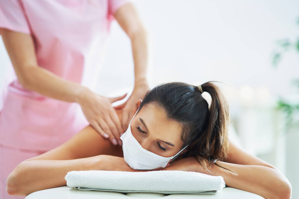 Volwassen vrouw met masker tijdens ontspannende massage in spa - Foto, afbeelding