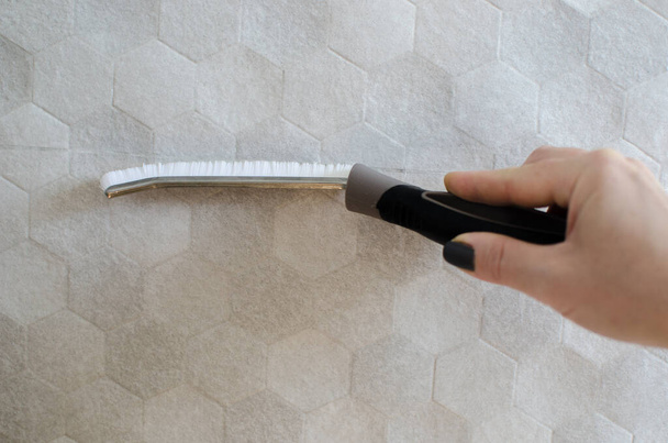 La mano de una mujer sostiene un cepillo para limpiar las juntas de azulejos. Cepillo estrecho para lugares de difícil acceso. Pinte el pincel sobre un fondo gris aislado. Costuras y grietas de limpieza. - Foto, imagen