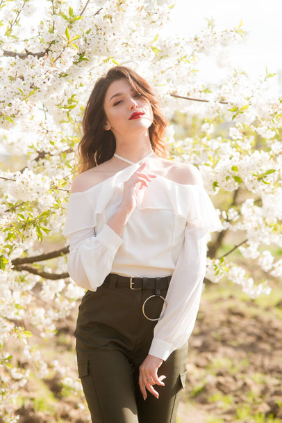 Lovely young girl in a white romantic silk blouse in spring in a blooming cherry garden in sunny weather. Spring and Fashion - Foto, immagini