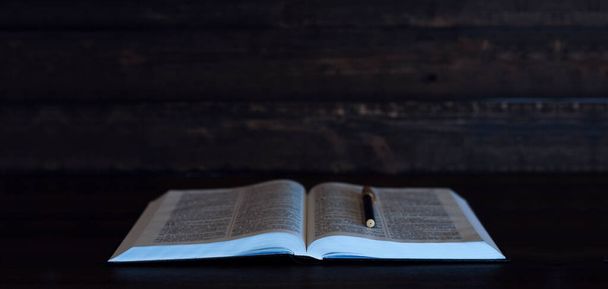 Das alte Buch Heilige Bibel aufschlagen. Stift auf dem Buch. Im Dunkeln auf einem hölzernen Hintergrund. - Foto, Bild