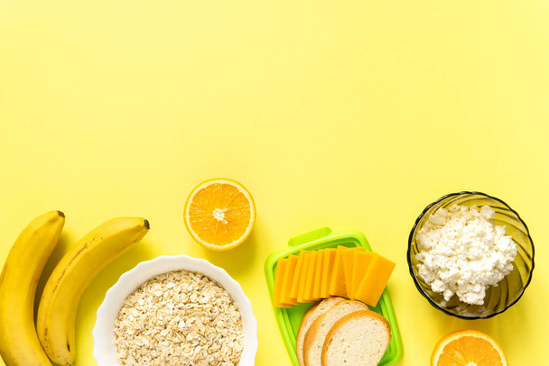 Ingredients for healthy breakfast. Oatmeal, dairy products and fruits on yellow background, top view - Photo, Image