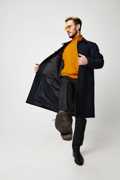 Paltolu ve pantolonlu şık bir adam ve dans eden turuncu süveter bahar modası yeni kıyafetler. - Fotoğraf, Görsel