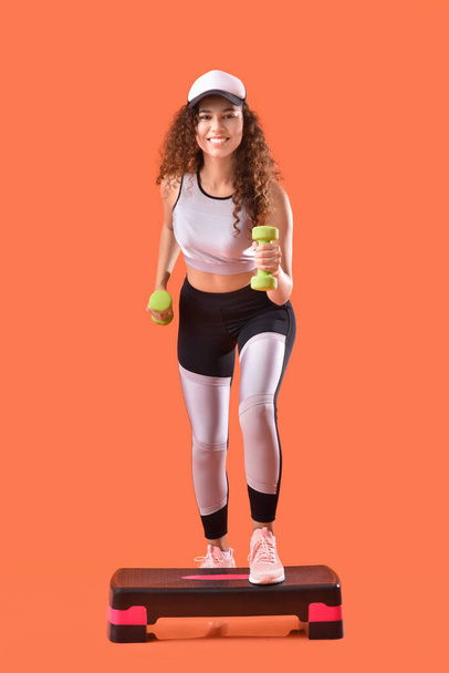 Schöne junge Frau trainiert mit Kurzhanteln auf farbigem Hintergrund - Foto, Bild