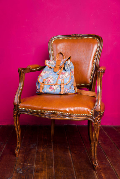 Hátizsák karosszéken, minimalista belsővel rózsaszín fallal és fapadlóval - Fotó, kép