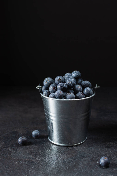 Fresh ripe blueberry in a metal small bucket on black background. Juicy blueberry berries full of vitamins. - Foto, imagen