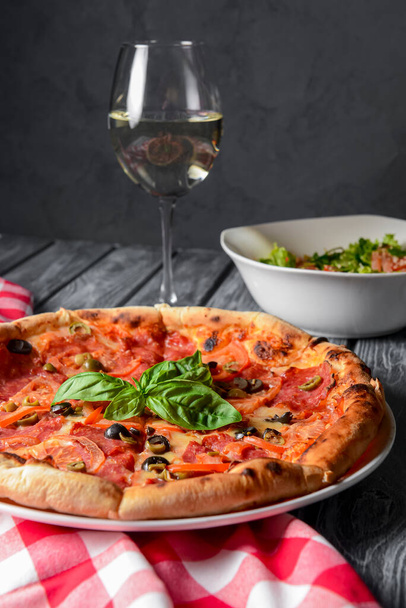 Fresh italian pizza with salami and black olives served with a glass of white wine. Traditional Italian pizza recipe, Italian cuisine. Close up on pizza. Fast food, junk food concept. - Φωτογραφία, εικόνα