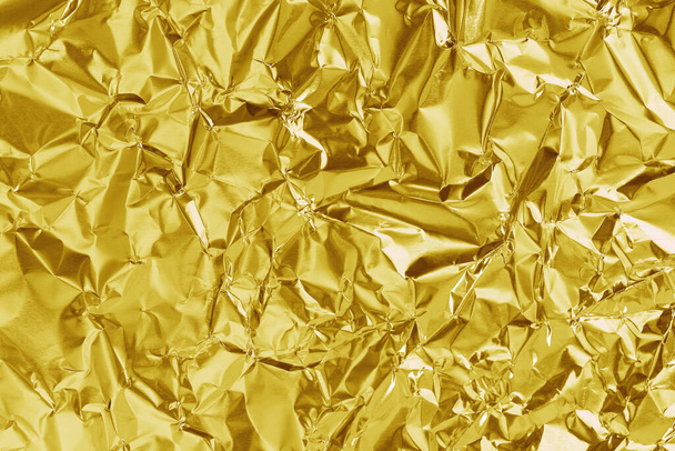 Glanzend goud folie textuur achtergrond, patroon van geel inpakpapier met verkreukeld en golvend. - Foto, afbeelding