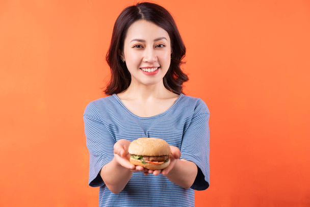 Young Asian woman holding hamburger on orange background - Zdjęcie, obraz