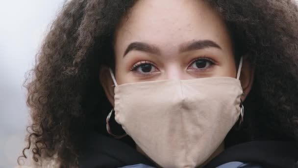 Gorgeous dark skinned black young woman with Afro hairstyle wearing protective mask from COVID virus, afrrican american girl with medical respirstor standing outdoors in public space, lockdown concept - Video
