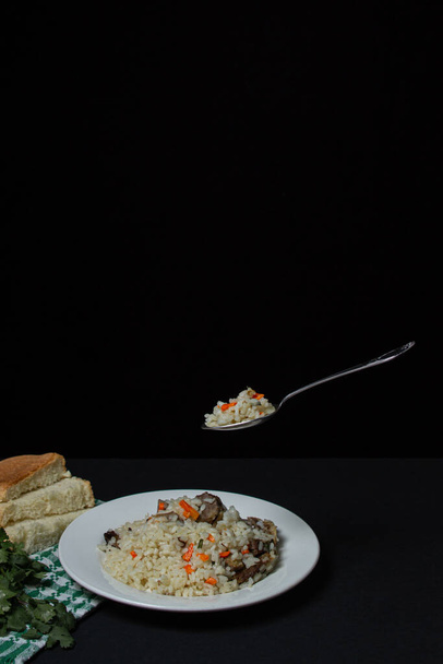 Pilaf su sfondo nero. Un cucchiaio di pilaf su un piatto. Fotografia di cibo creativo su sfondo scuro - Foto, immagini