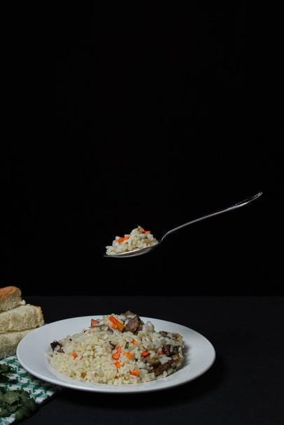 Πιλάφι σε μαύρο φόντο. Μια κουταλιά πιλάφι πάνω από ένα πιάτο. Δημιουργική φωτογραφία φαγητού σε σκούρο φόντο - Φωτογραφία, εικόνα