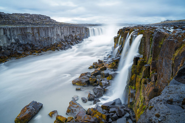 Longue exposition de la cascade Selfoss en Islande par un jour nuageux et pluvieux. Rivière sauvage coule entre les falaises abruptes de basalte. Paysage volcanique islandais. - Photo, image
