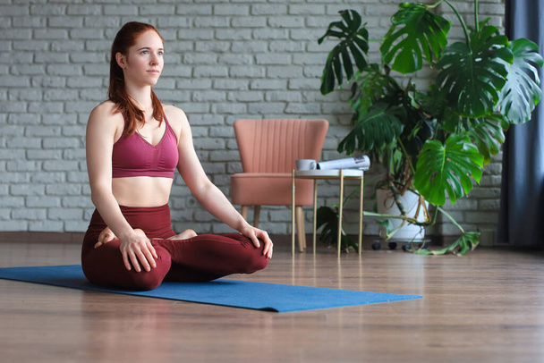 Beautiful woman sitting in lotus pose and meditating at yoga studio - Фото, зображення