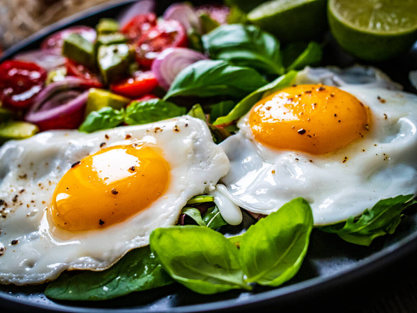 Sunny side up eggs with avocado, cherry tomatoes, toasted bread and red onion on wooden table  - Foto, Imagem