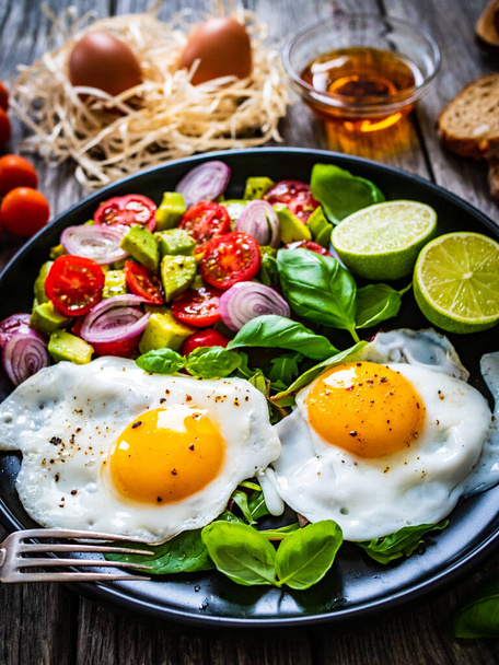 Sunny side up eggs with avocado, cherry tomatoes, toasted bread and red onion on wooden table  - Fotoğraf, Görsel