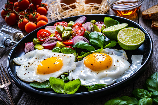 Sunny side up eggs with avocado, cherry tomatoes, toasted bread and red onion on wooden table  - Фото, зображення