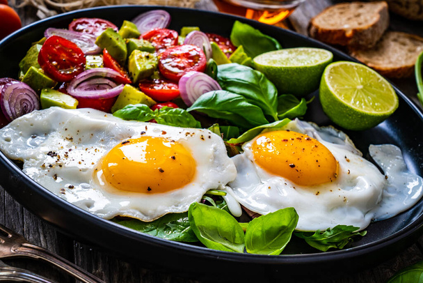 Sunny side up eggs with avocado, cherry tomatoes, toasted bread and red onion on wooden table  - Foto, Bild