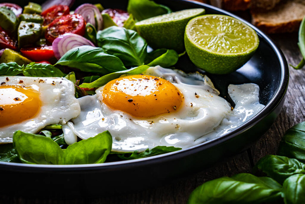Sunny side up eggs with avocado, cherry tomatoes, toasted bread and red onion on wooden table  - Foto, afbeelding
