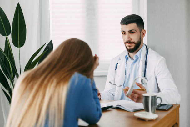 A serious male doctor of oriental appearance consults the patient, shows information about her illness and talks about the medical examination. - Valokuva, kuva