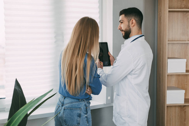 A friendly male doctor of oriental appearance advises the patient, shows information about her illness and tells about the medical examination. - Photo, Image
