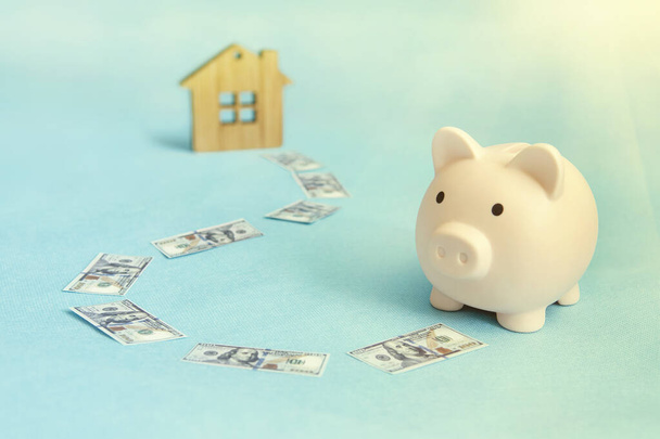 El concepto de ahorrar dinero para comprar un apartamento, casa u otra propiedad residencial. Hucha y casa de madera sobre fondo azul. - Foto, Imagen