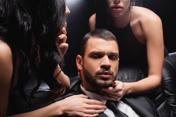 sensual women seducing young businessman on black background - Photo, Image