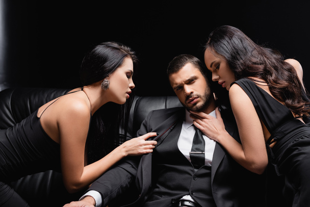 successful businessman near passionate women seducing him on leather couch on black - Photo, Image