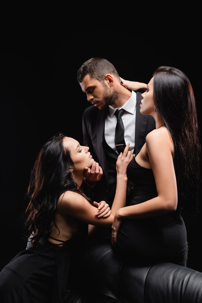 страстные, элегантные женщины соблазняют мужчину в костюме, изолированном от черного - Фото, изображение