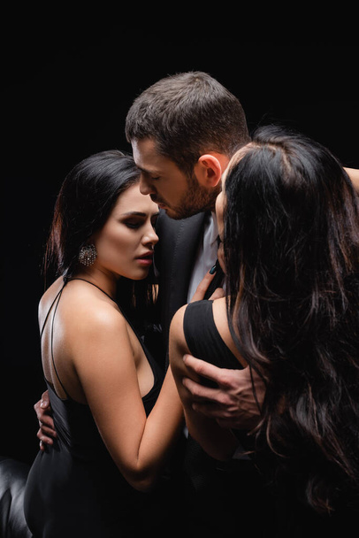 young man embracing brunette women isolated on black - Photo, Image