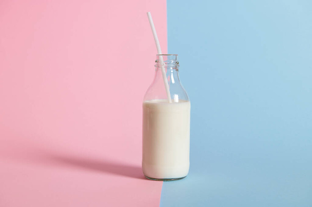 Studyjne ujęcie butelki ze świeżym mlekiem ze słomką na bicolor różowym i niebieskim tle. Przestrzeń kopiowania - Zdjęcie, obraz