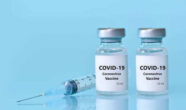 Twee flacons met een vaccin, een spuit op een blauwe achtergrond.Het concept van geneeskunde, gezondheidszorg en wetenschap.Coronavirusvaccin.Kopieer ruimte voor tekst.. - Foto, afbeelding