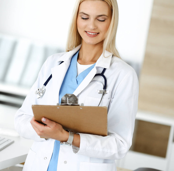 Doctor woman at work in hospital controls medication history records and exam results while using clipboard. Medicine and healthcare concept - Foto, imagen