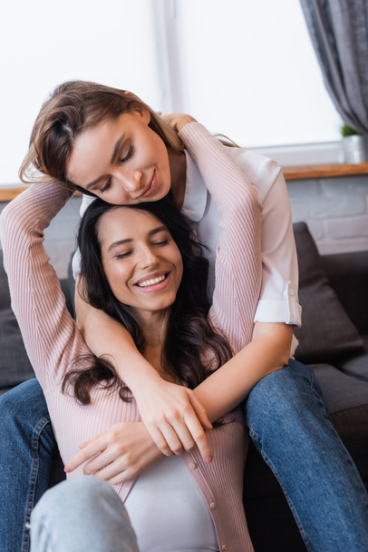 smiling lesbians with closed eyes hugging in living room - Foto, Imagem