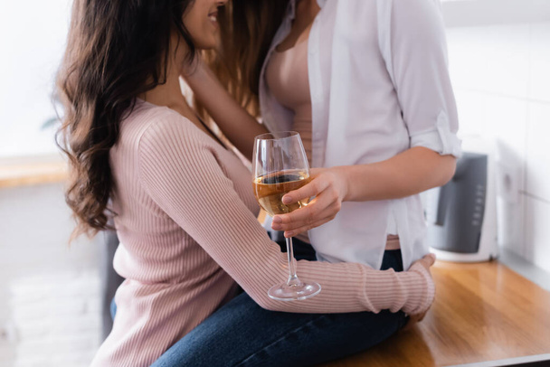 cropped view of woman sitting on table and holding glass of wine near happy girlfriend  - Foto, Imagen