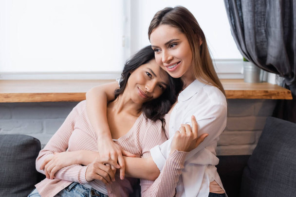 smiling lesbian woman embracing happy girlfriend in living room - Photo, image