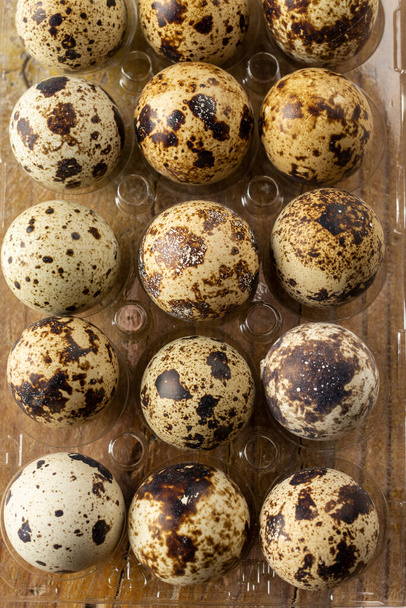 Vista aérea de huevos de codorniz en taza de huevo de plástico transparente, enfoque selectivo, en mesa de madera, vertical - Foto, Imagen