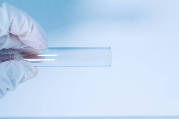 Medical laboratory. A gloved hand holds an empty test tube against a blue background. Close-up. - Foto, afbeelding