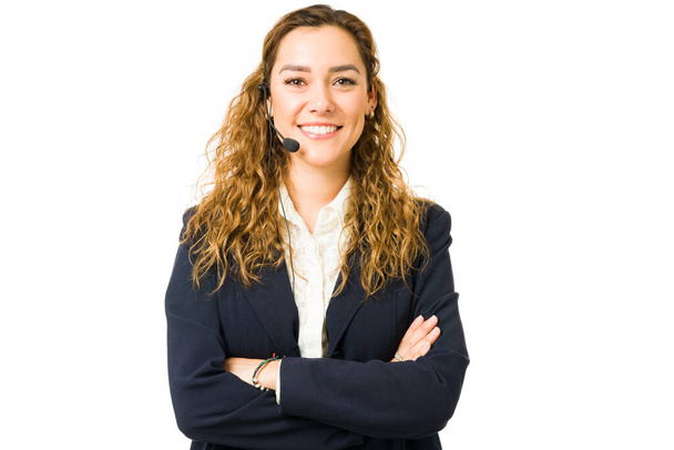 Портрет профессиональной молодой женщины, улыбающейся и работающей продавцом. Латиноамериканка в возрасте 20 лет носит наушники со скрещенными руками - Фото, изображение