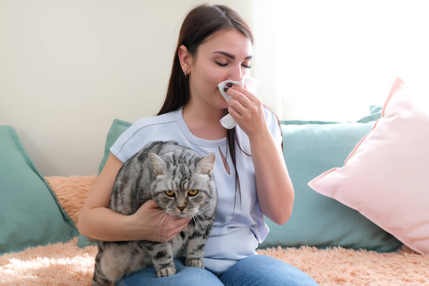 young woman is sneezing from fur allergy on the sofa and playing with her cat. - Fotoğraf, Görsel
