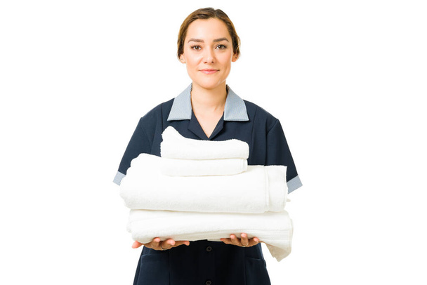 Retrato de una atractiva mujer latina de unos 20 años trabajando como empleada de limpieza de un hotel. Camarera hispana sosteniendo toallas limpias y frescas - Foto, Imagen