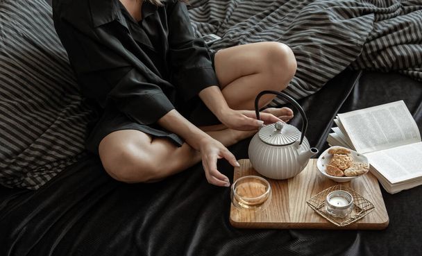 Kobieta je śniadanie z herbatą i ciasteczkami, leżąc w łóżku w wolny dzień. - Zdjęcie, obraz