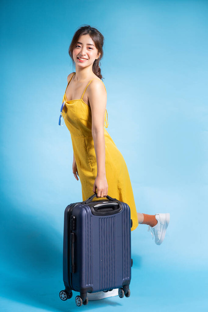 Joven mujer asiática sosteniendo maleta sobre fondo azul, concepto de verano - Foto, Imagen
